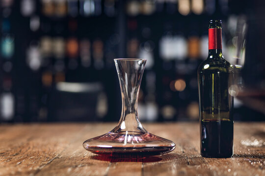 Red wine in bottle and decanter stands on wooden table in restaurant, dark background