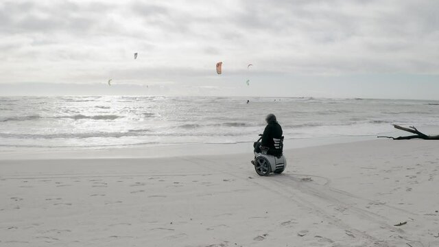 WS POV SLO MO Man in motorized wheelchair looking at people kiteboarding on sea / Livorno, Tuscany, Italy