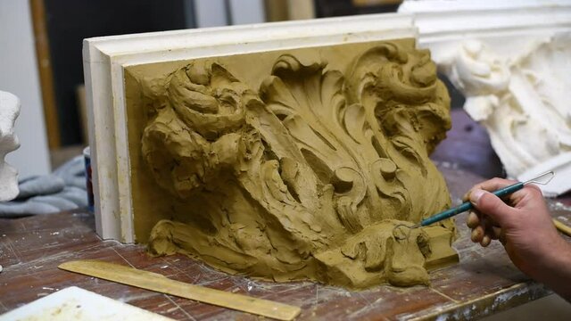 Sculptor create clay model of a Corinthian capitel with scrolls and unfurled acanthus leaves in restoration workshop