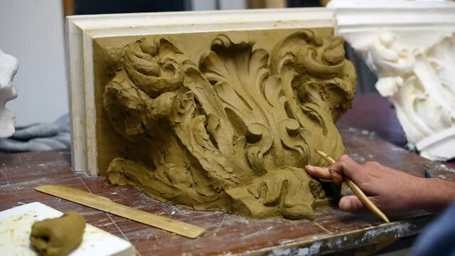 Sculptor create clay model of a Corinthian capitel with scrolls and unfurled acanthus leaves in restoration workshop