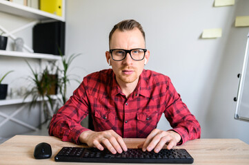Webcam view of concentrated young attractive man in casual wear, he is typing on the keyboard with...