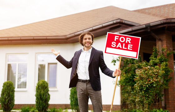 Positive property manager holding FOR SALE sign near residential building outside