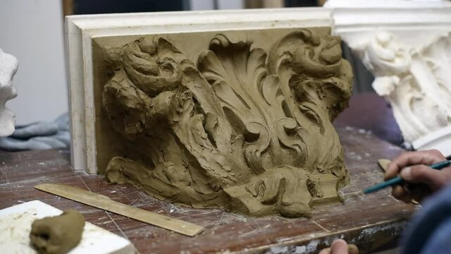 Sculptor create clay model of a Corinthian capitel with scrolls and unfurled acanthus leaves in restoration workshop