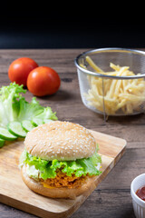 Crispy fried chicken burger on Wood Cutting board with french fries and ketchup on wooden background.