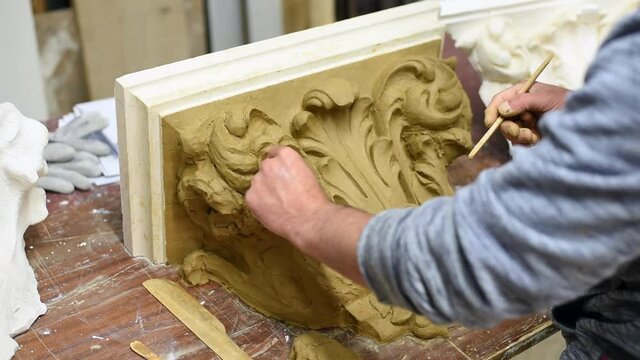 Sculptor create clay model of a Corinthian capitel with scrolls and unfurled acanthus leaves in restoration workshop