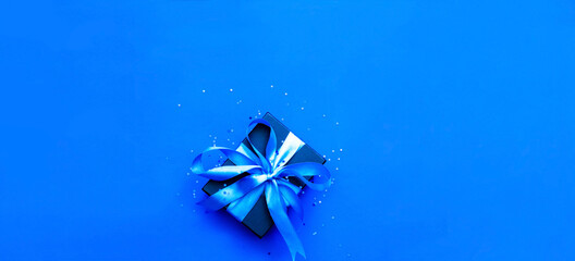 Black gift box on blue background with sparkles. Festive concept. Creative copy space for projects and design.