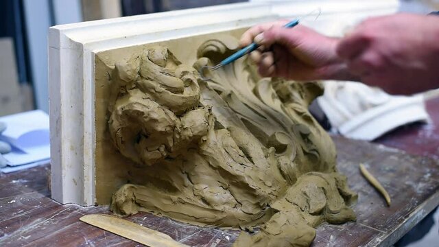 Sculptor create clay model of a Corinthian capitel with scrolls and unfurled acanthus leaves in restoration workshop
