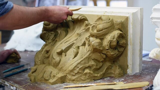 Sculptor create clay model of a Corinthian capitel with scrolls and unfurled acanthus leaves in restoration workshop