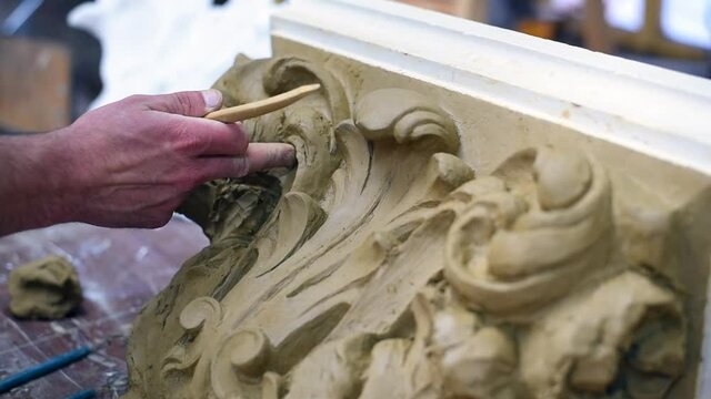 Sculptor create clay model of a Corinthian capitel with scrolls and unfurled acanthus leaves in restoration workshop