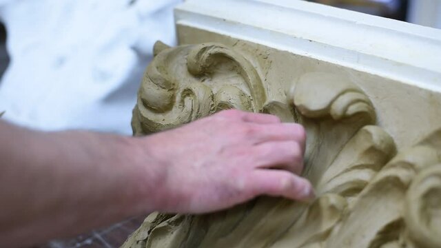 Sculptor create clay model of a Corinthian capitel with scrolls and unfurled acanthus leaves in restoration workshop