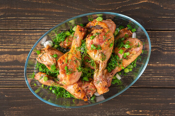 Baked chicken drumsticks with rosemary, spices, onions and dill on a wooden background , top view