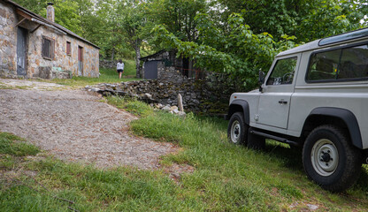 mountain trail with a parked beige All-terrain car and a person walking.
