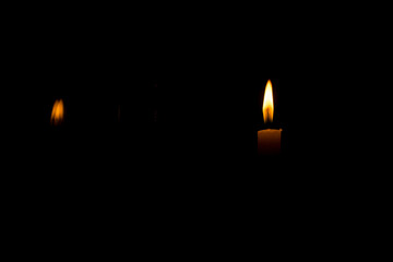 A lit candle in a dark room with reflection of the flame on glass
