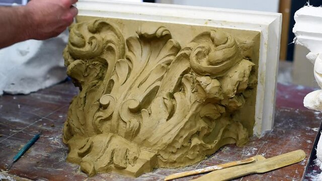 Sculptor create clay model of a Corinthian capitel with scrolls and unfurled acanthus leaves in restoration workshop