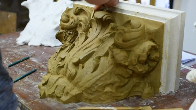 Sculptor create clay model of a Corinthian capitel with scrolls and unfurled acanthus leaves in restoration workshop