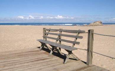 Fototapeta na wymiar Banco de madeira num passadiço à entrada de uma praia com vista para o horizonte num dia quente de verão