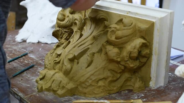 Sculptor create clay model of a Corinthian capitel with scrolls and unfurled acanthus leaves in restoration workshop