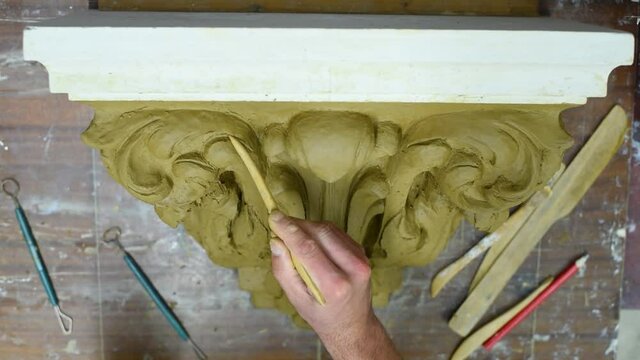 Sculptor create clay model of a Corinthian capitel with scrolls and unfurled acanthus leaves in restoration workshop