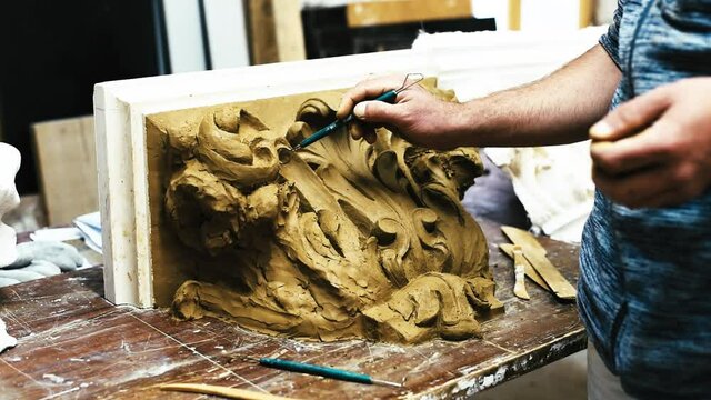 Sculptor create clay model of a Corinthian capitel with scrolls and unfurled acanthus leaves in restoration workshop