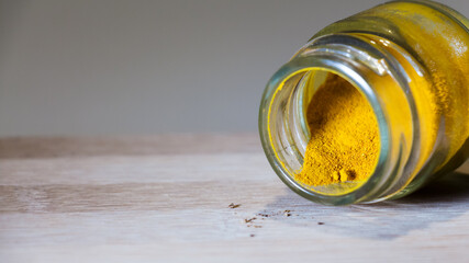 Pequeño recipiente de vidrio con cúrcuma dentro aislado sobre una tabla de madera con luz directa...