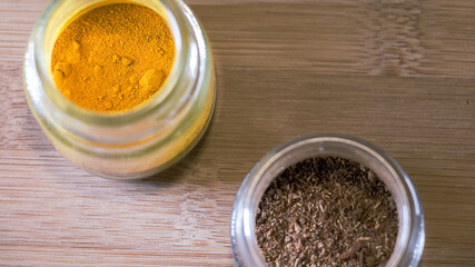 Vista desde arriba de pequeños recipientes de vidrio con cúrcuma y comino dentro aislados sobre una tabla de madera