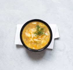 Vegetable soup of cabbage, potatoes, carrots with dill on a bowl on a light gray background top view