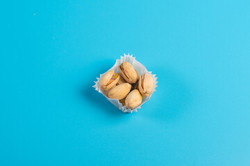 A serving of pistachios in a paper muffin cup on a blue background.