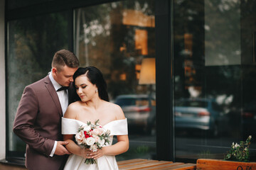 Bride and groom. Close up portrait of a man in a suit and brunette woman in a white wedding dress. In the city against the backdrop of a shop window, on the wedding day. European appearance. 
