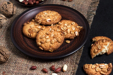 Homemade peanut cookies on a brown plate with raw peanuts in background