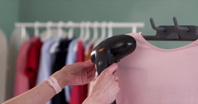 Close up, a woman steams a t-shirt with a steamer.
