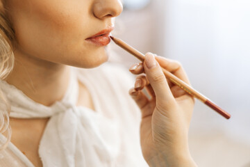 Close-up of professional make-up artist making makeup young unrecognizable woman lips with lip pencil in beauty salon. Concept of beauty, fashion and stylish makeup.