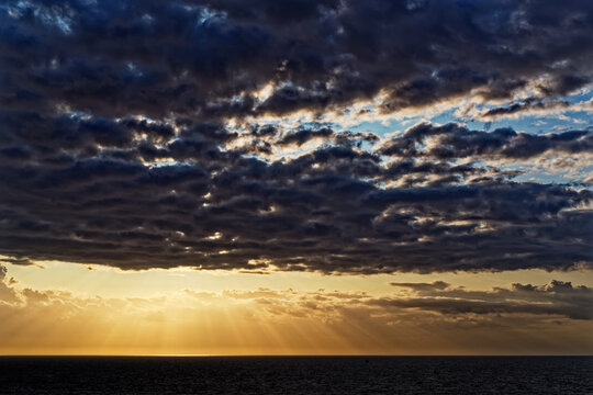 Beautiful dark clouds and golden sun rays above sea during sunset