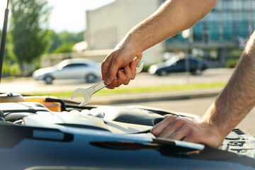 A man holds a wrench over a car engine. Car inspection