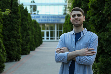 Young man in shirt with folded hands against university. Study