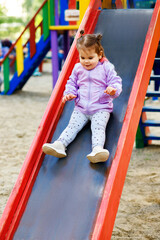 a little girl descends from a children's slide in the yard of her house, a colorful playground, a...