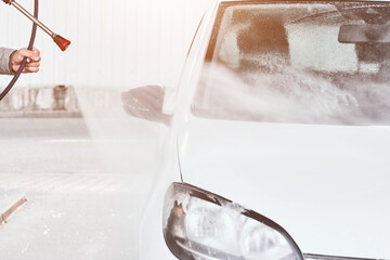 Close up mans hand washing a white car using high pressure water. Car self washing service 