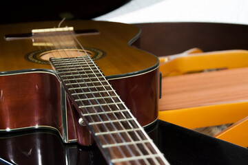 Acoustic Guitar lying down over the grand piano showing piano strings