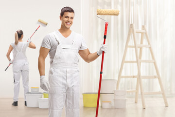 Male painter with a paint roller posing and a female painter painting a wall