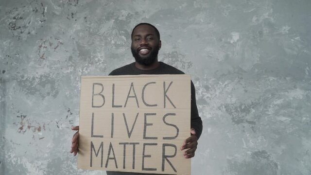 handsome african american man smiling and showing banner with slogan "black lives matter"