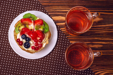 Home made cake with cream and fruit and hot tea on wooden table.