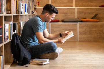 Young male student read and learns by the book shelf at the library.Reading a book.	
