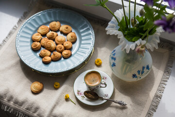 Delicate porcelain coffee set with espresso and homemade cookies, spoon and spring flowers on linen fabric.