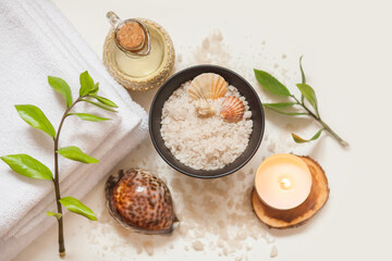 Towel, cosmetic massage oil, leaves, sea salt with shells and candle. Top view, flat lay on white background. Spa, beauty and wellness concept