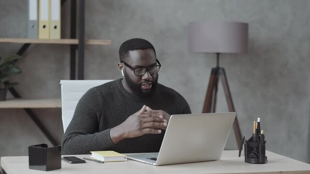 black guy waves his hand into a laptop and communicates via video link with loved ones in casual clothes at home\ oficce