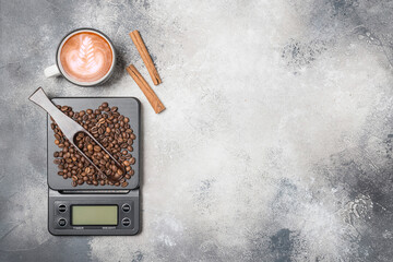 Top view of a Cup of coffee on a table, kitchen scale with coffee beans and wooden spoon,  sugar and cinnamon sticks