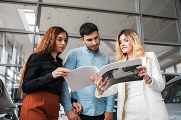 Car saleswoman shows catalog 
to buyers. Young couple chooses a new car