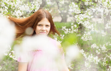 Fototapeta premium red-haired teen girl having fun in a blooming cherry orchard, the concept of spring and the end of the quarantine