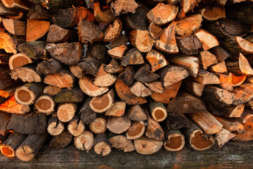 Firewood background. Preparation of firewood for the winter and use for cooking. Stacks of firewood with sun spots.