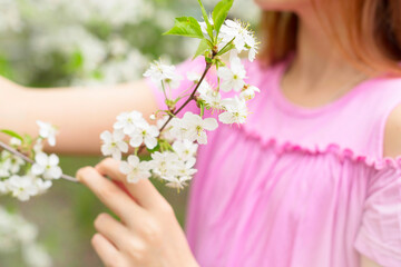Fototapeta premium a girl in protective face mask stands near blossoming cherry tree during quarantine due to the coronavirus pandemic