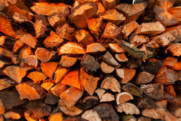 Firewood background. Preparation of firewood for the winter and use for cooking. Stacks of firewood with sun spots.